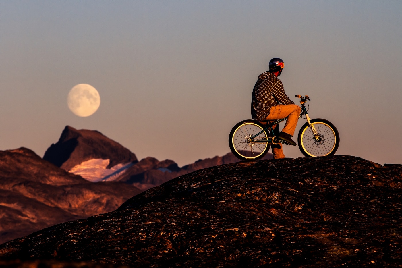 Red Bull trial biker Petr Kraus and the full moon at sunset in Kangaamiut in Greenland. Photo by Mads Pihl - Visit Greenland
